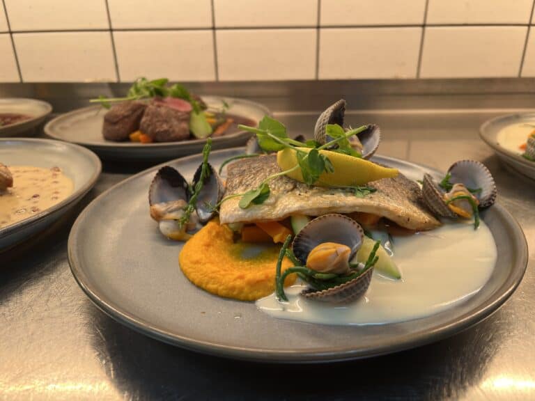 Gegrilde vis met groenten en saffraan mayonaise op een bord.